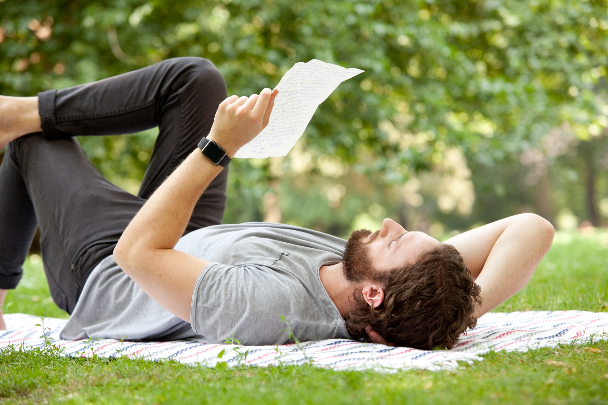 Man lying on blanket in a park reading a letter