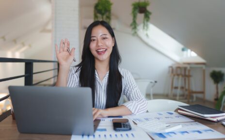 Asian businesswoman waving at someone during a video call in her bright office