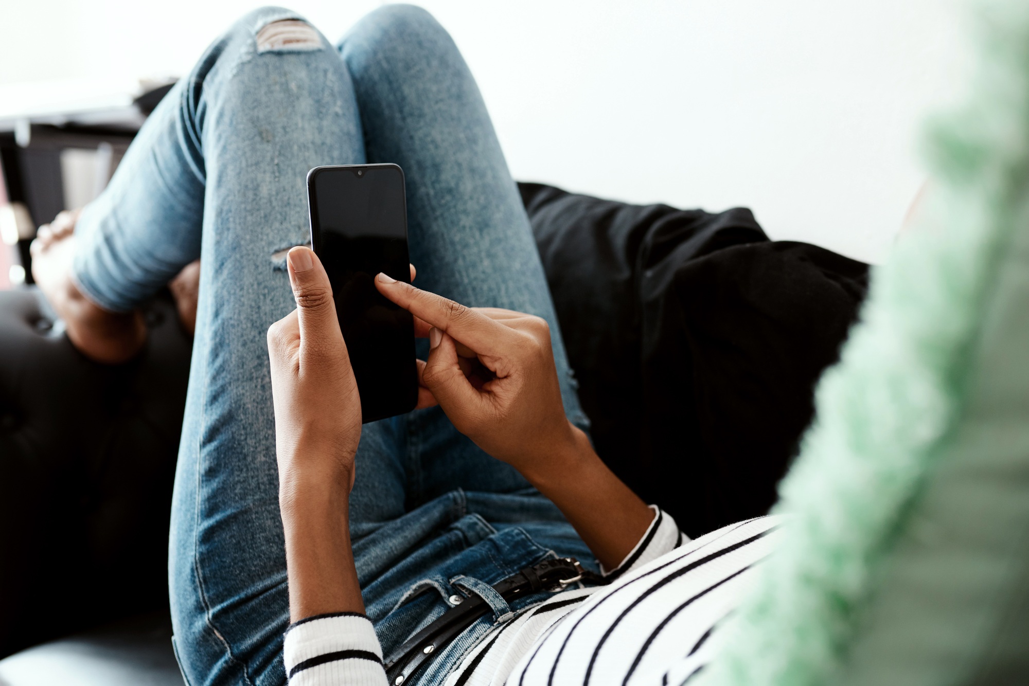 And send...Cropped shot of a woman using a smartphone on the sofa at home.