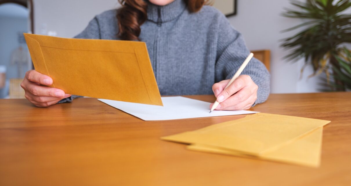 Closeup image of a woman writing on a letter and envelopes