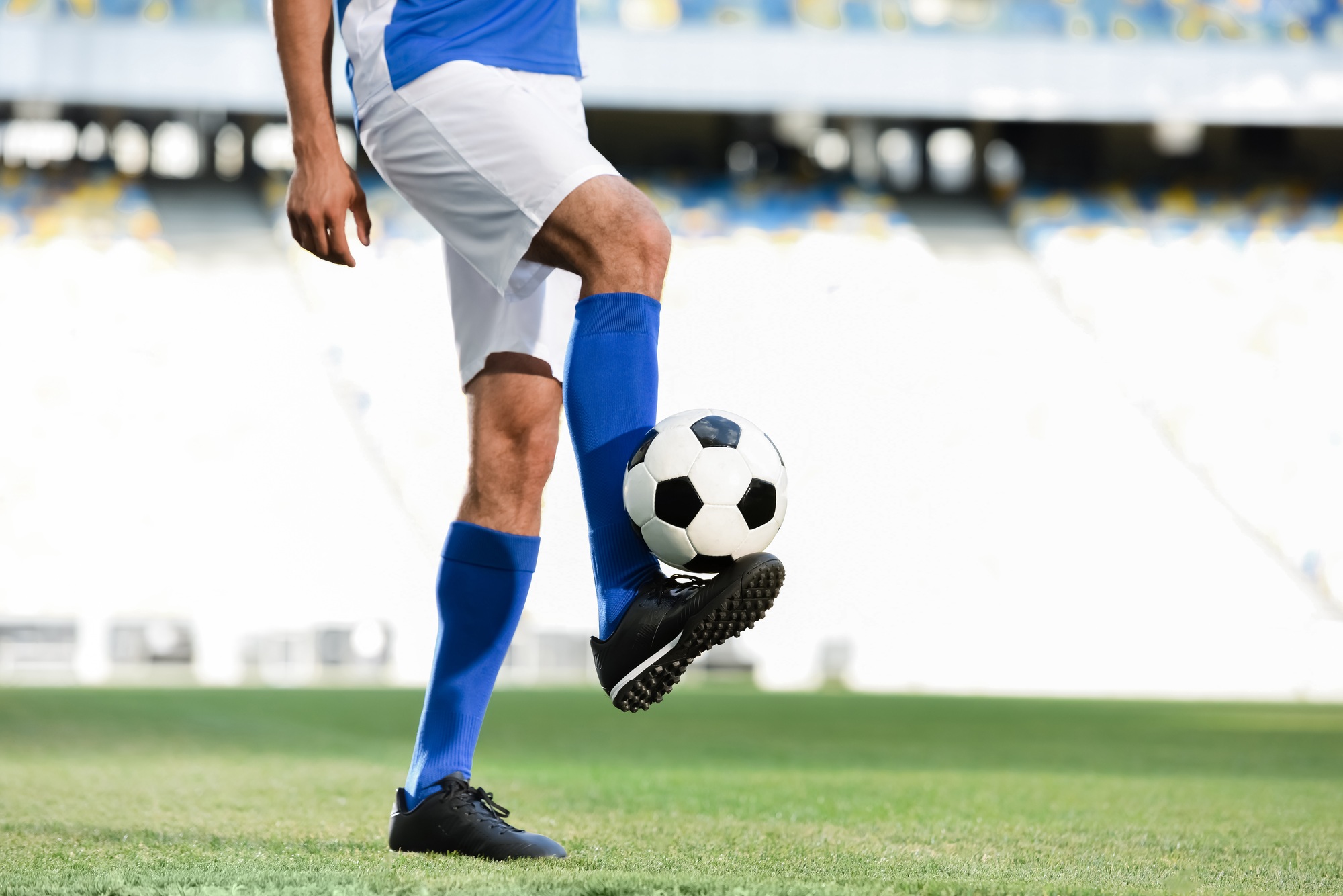 cropped view of professional soccer player in blue and white uniform playing with ball on football